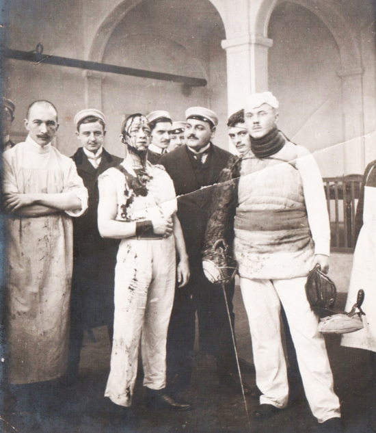 Due contendenti al termine della Mensur, con il medico pronto a suturare le ferite senza uso di anestetico, come previsto dal rituale (Germania, 1905 – Collezione Nautilus).